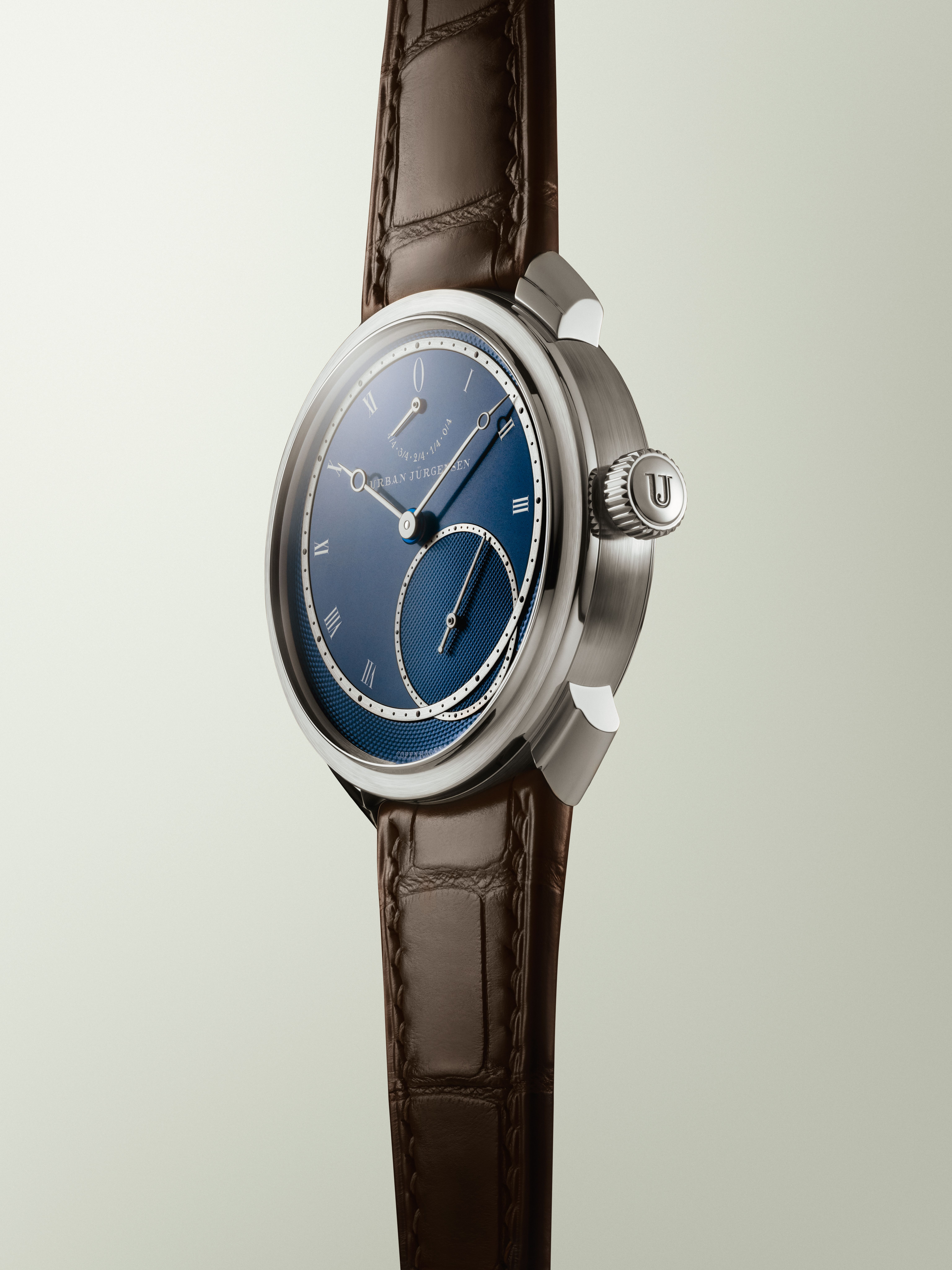 Platinum Urban Jürgensen wristwatch with blue guilloché dial, silver Roman numerals, power reserve indicator, and brown leather strap.