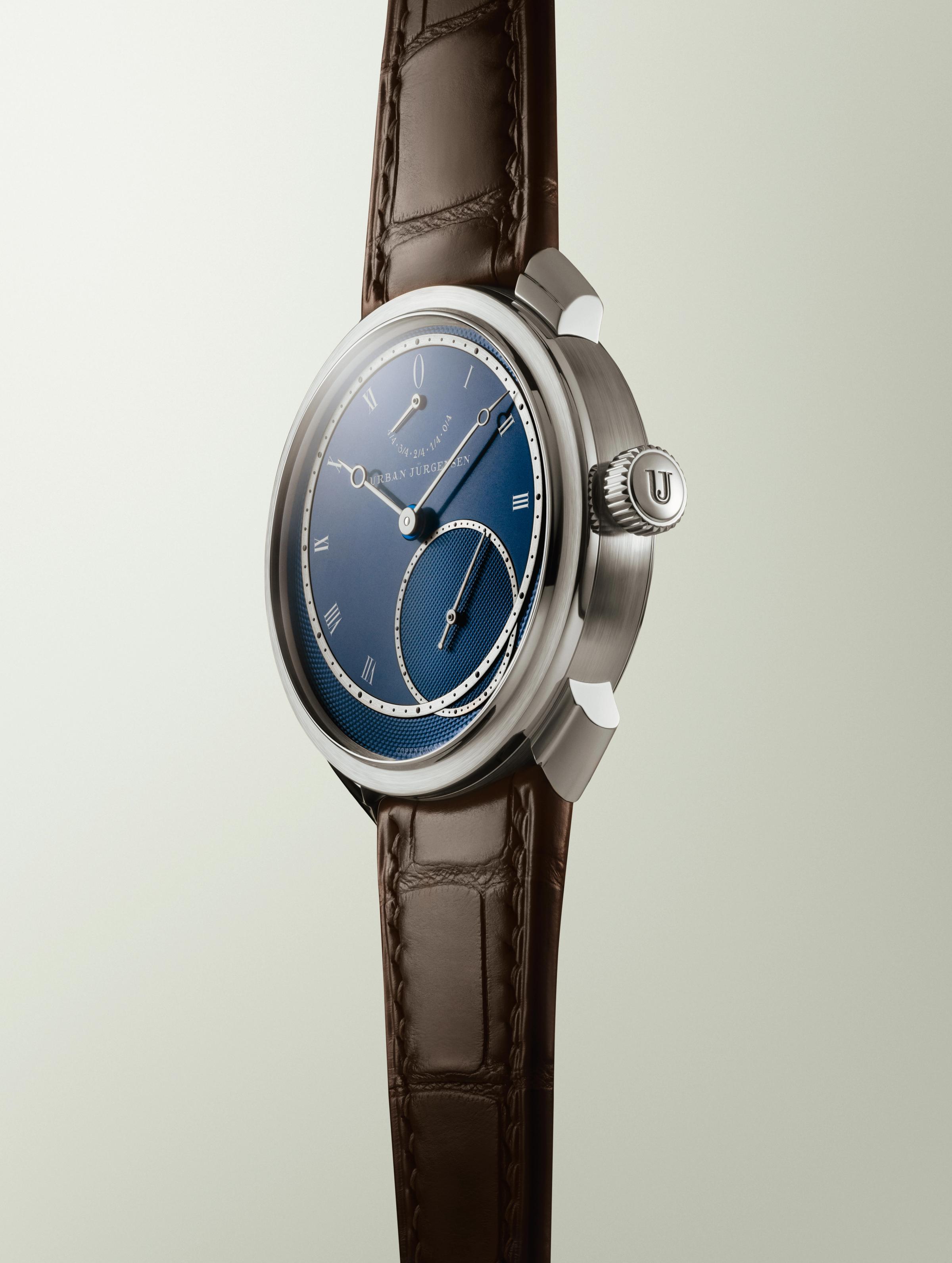 Platinum Urban Jürgensen wristwatch with blue guilloché dial, silver Roman numerals, power reserve indicator, and brown leather strap.