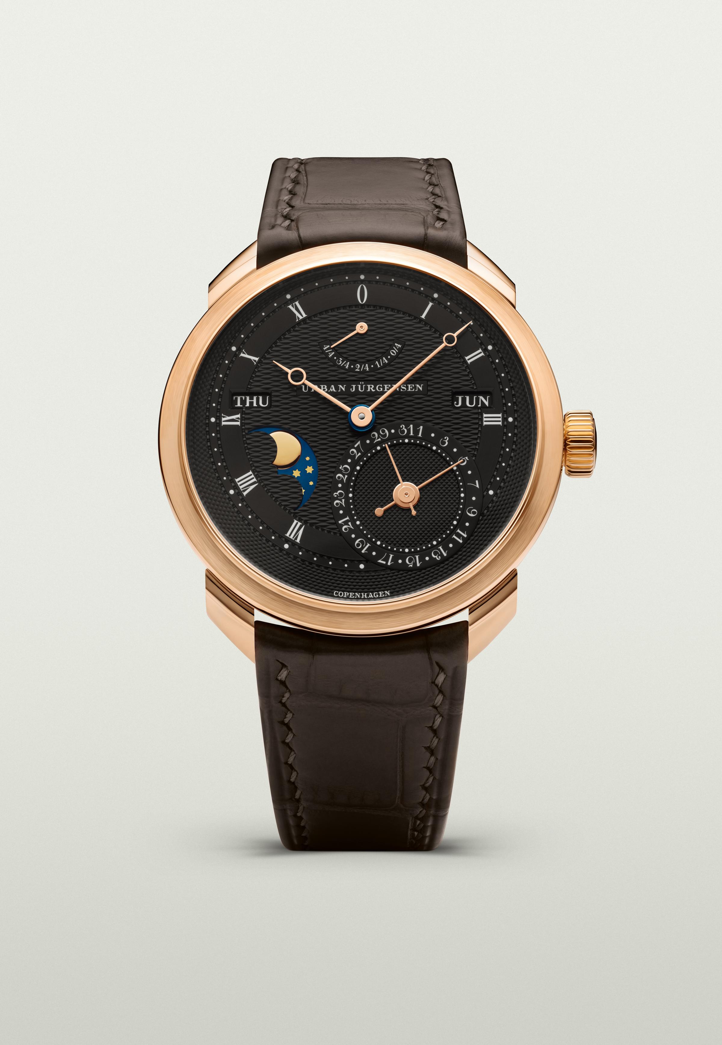 Rose gold Urban Jürgensen wristwatch with dark guilloché dial, moonphase, day and date indicators, power reserve display, and brown leather strap.