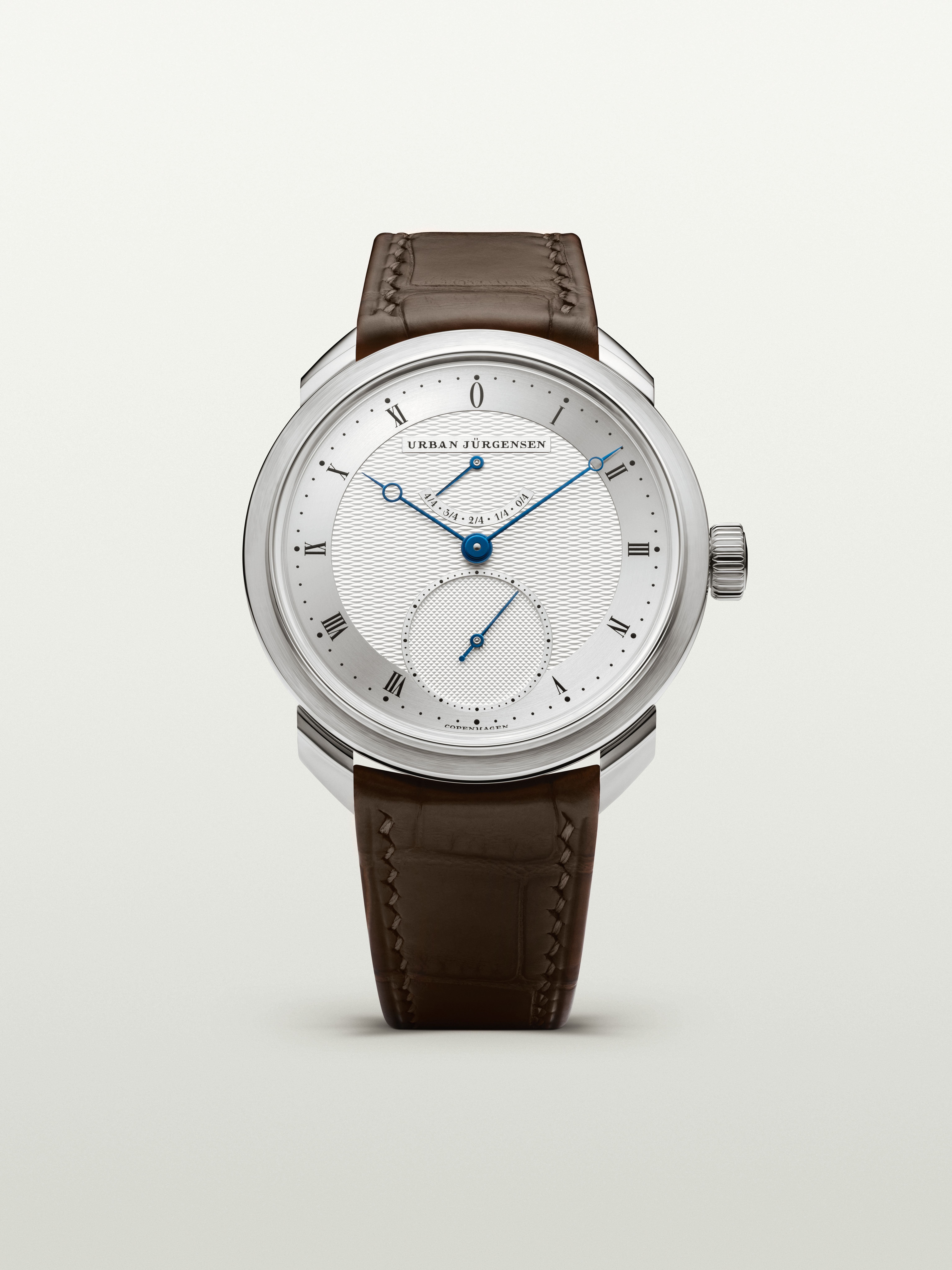 Platinum Urban Jürgensen watch with silver guilloché dial, blued hands, power reserve indicator, and brown leather strap.