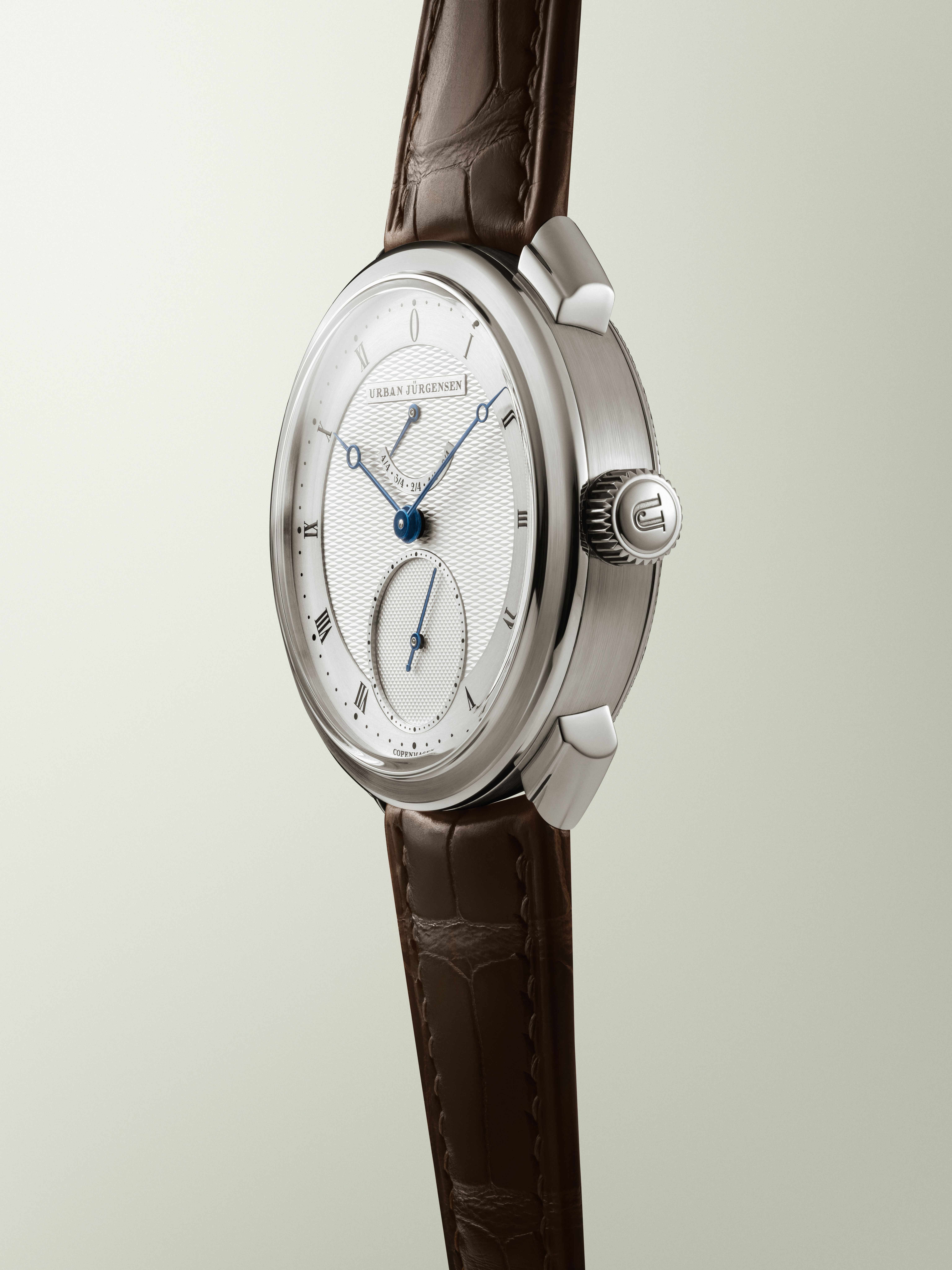 Urban Jürgensen wristwatch with guilloché dial, blue hands, Roman numerals, small seconds subdial, and power reserve indicator.