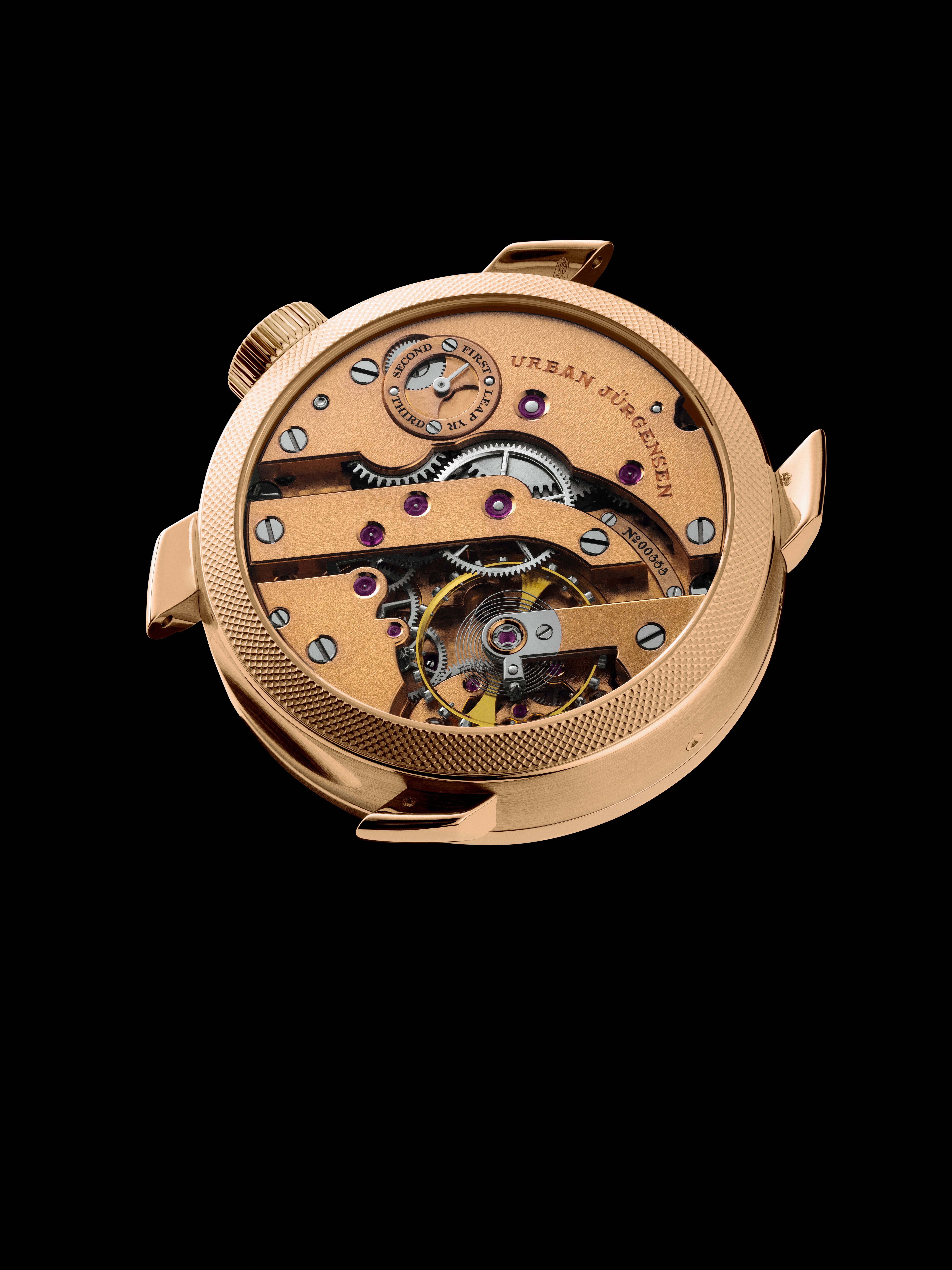 Reverse view of a rose gold Urban Jürgensen watch case showing the mechanical movement with engraved leap year indicator, ruby jewels, and visible tourbillon.