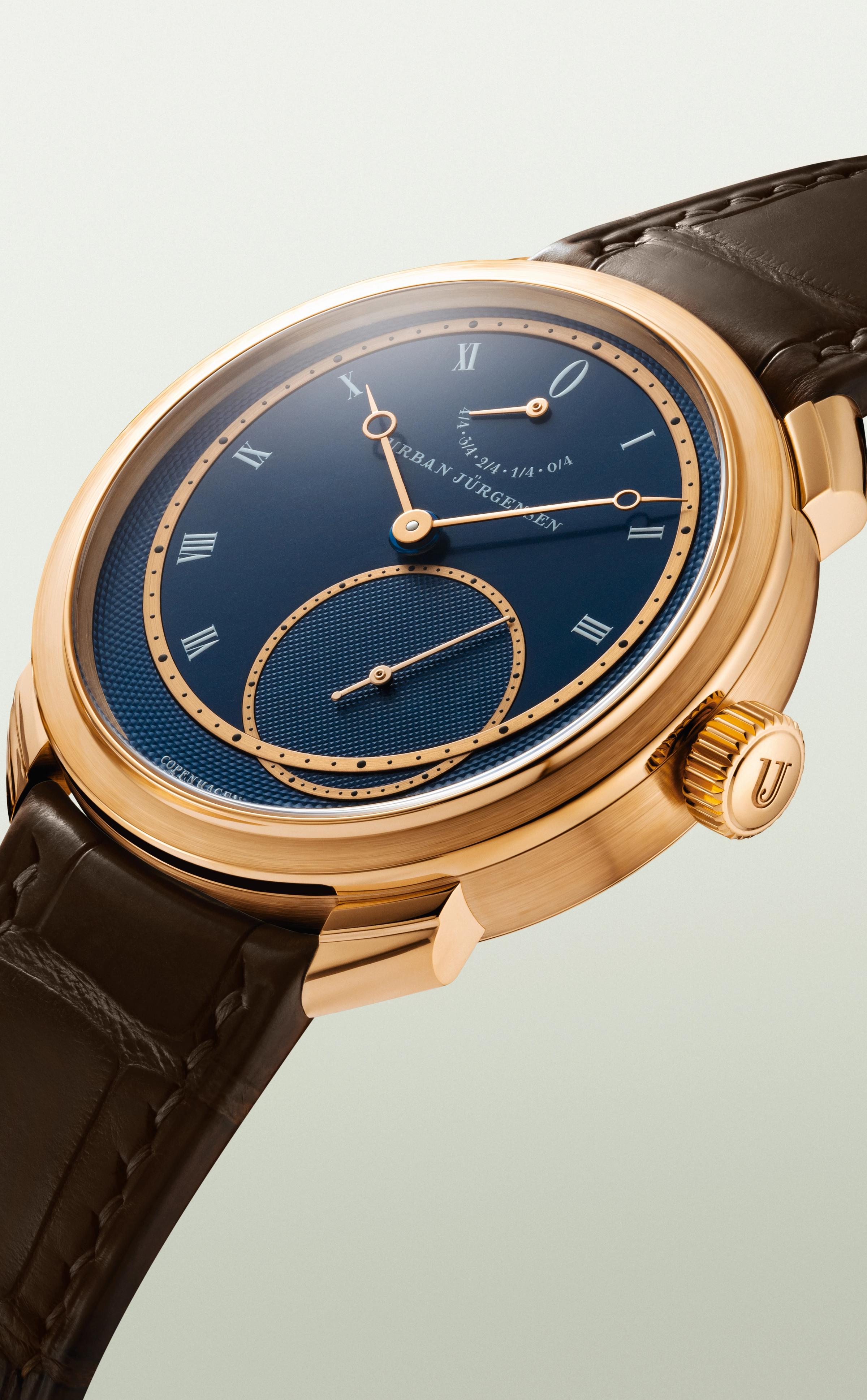 Rose gold Urban Jürgensen wristwatch with deep blue guilloché dial, Roman numerals, power reserve indicator, and brown leather strap.