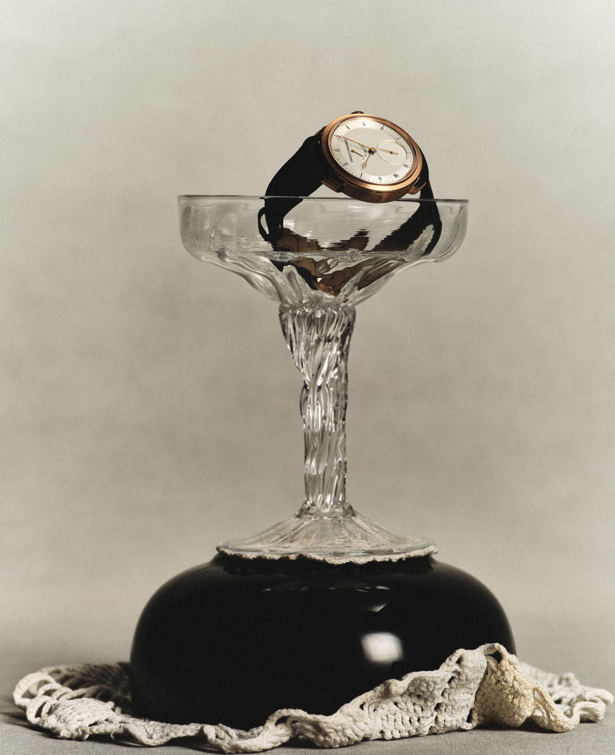 Urban Jürgensen wristwatch with a white dial and black strap, elegantly displayed inside an inverted glass coupe resting on a black base with lace detailing.