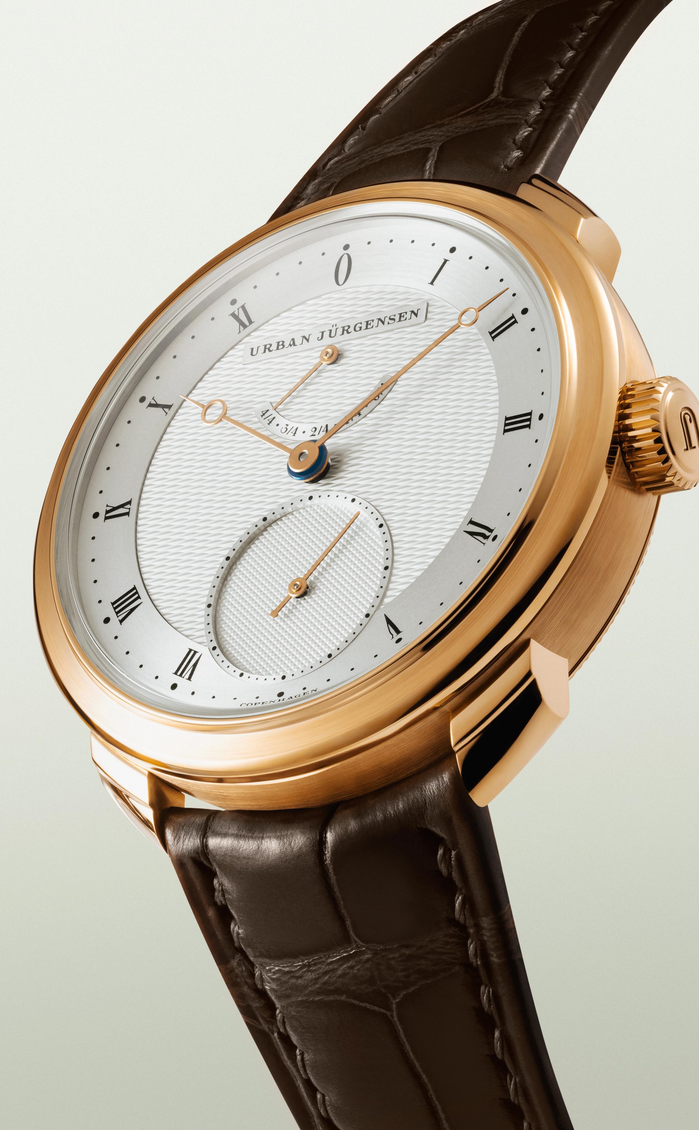 Rose gold Urban Jürgensen watch with guilloché silver dial, gold hands, power reserve, and brown leather strap.