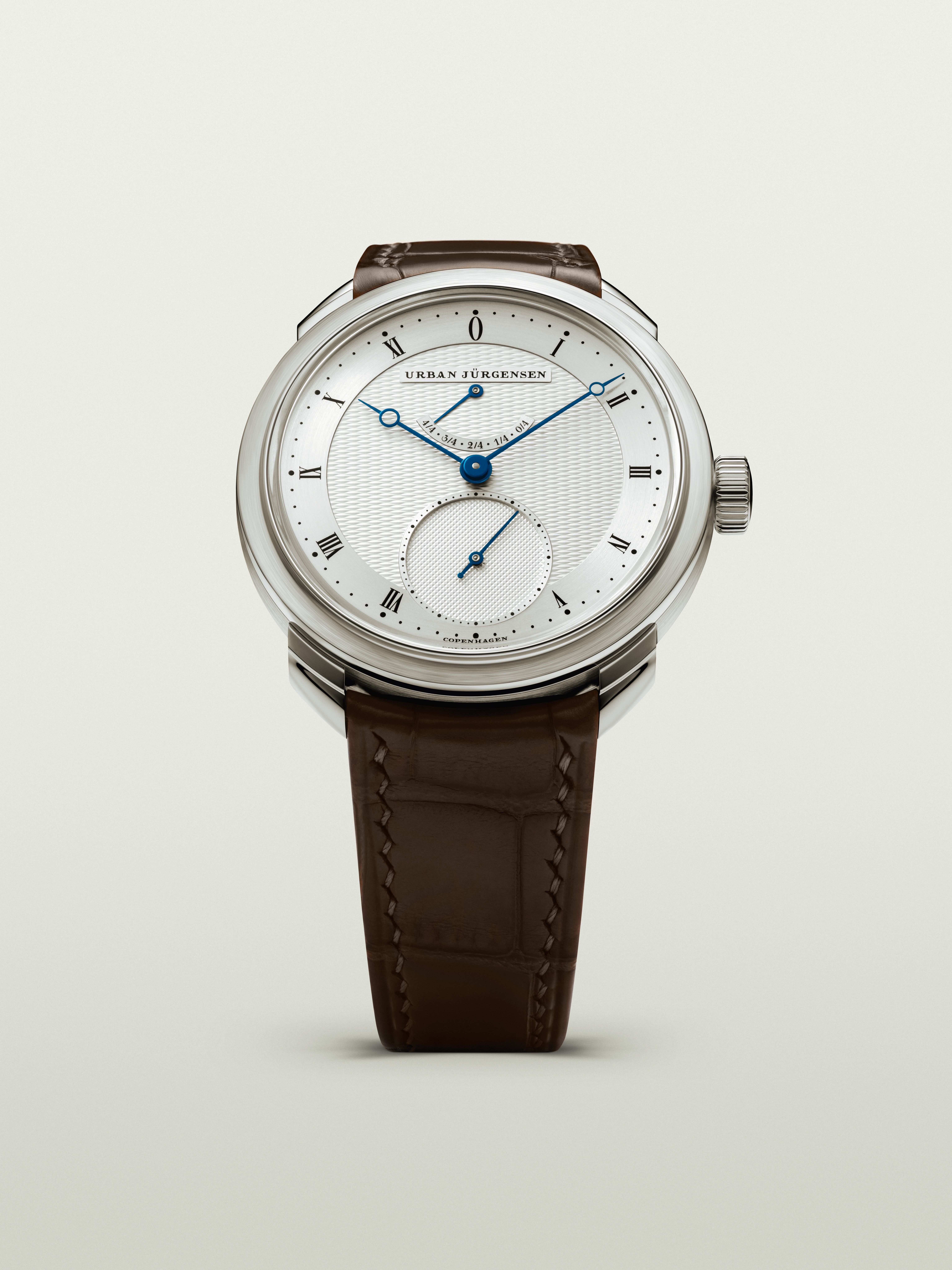 Platinum Urban Jürgensen watch with silver guilloché dial, blued hands, power reserve indicator, and brown leather strap.