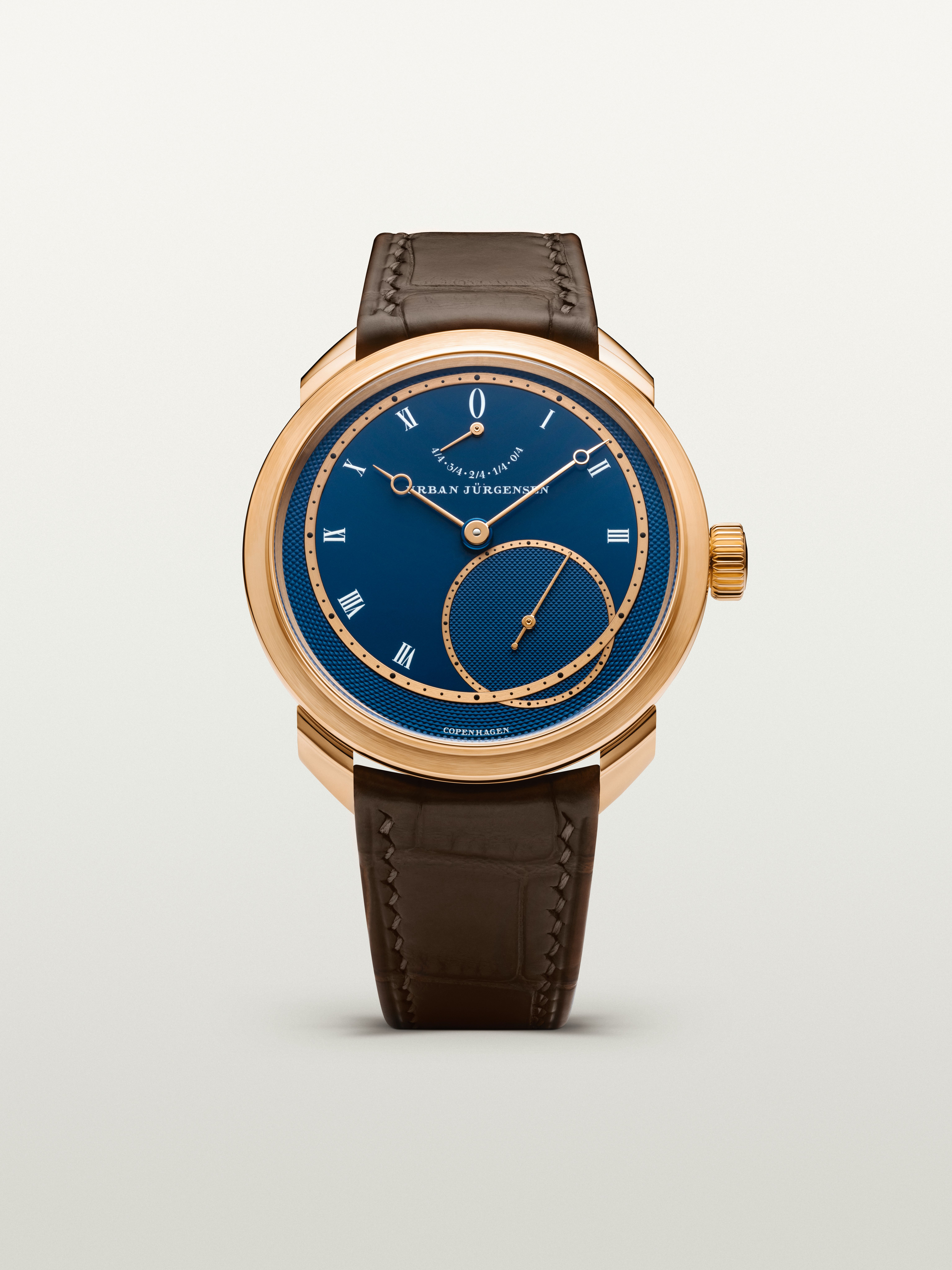 Rose gold Urban Jürgensen wristwatch with deep blue guilloché dial, Roman numerals, power reserve indicator, and brown leather strap.