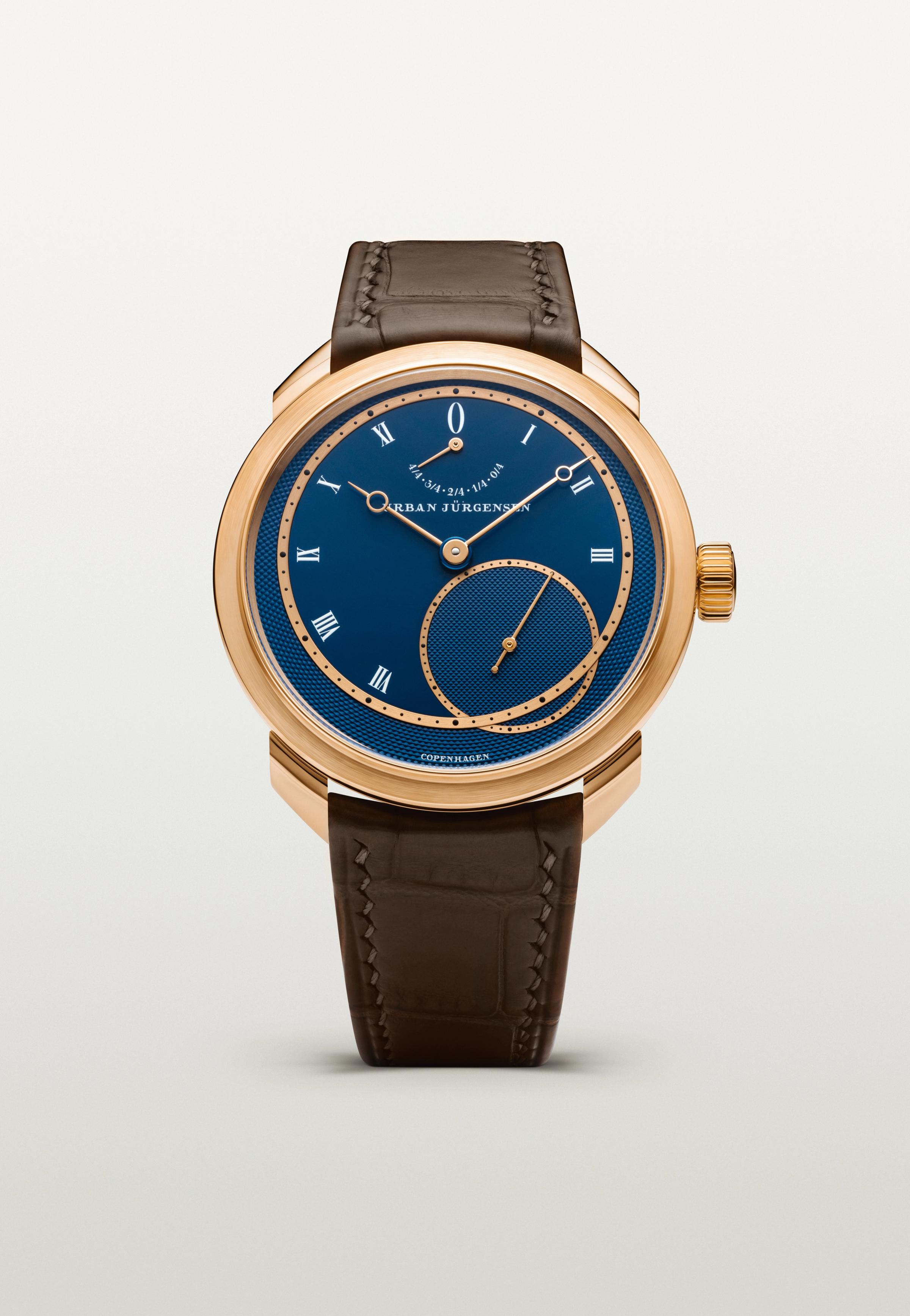 Rose gold Urban Jürgensen wristwatch with deep blue guilloché dial, Roman numerals, power reserve indicator, and brown leather strap.