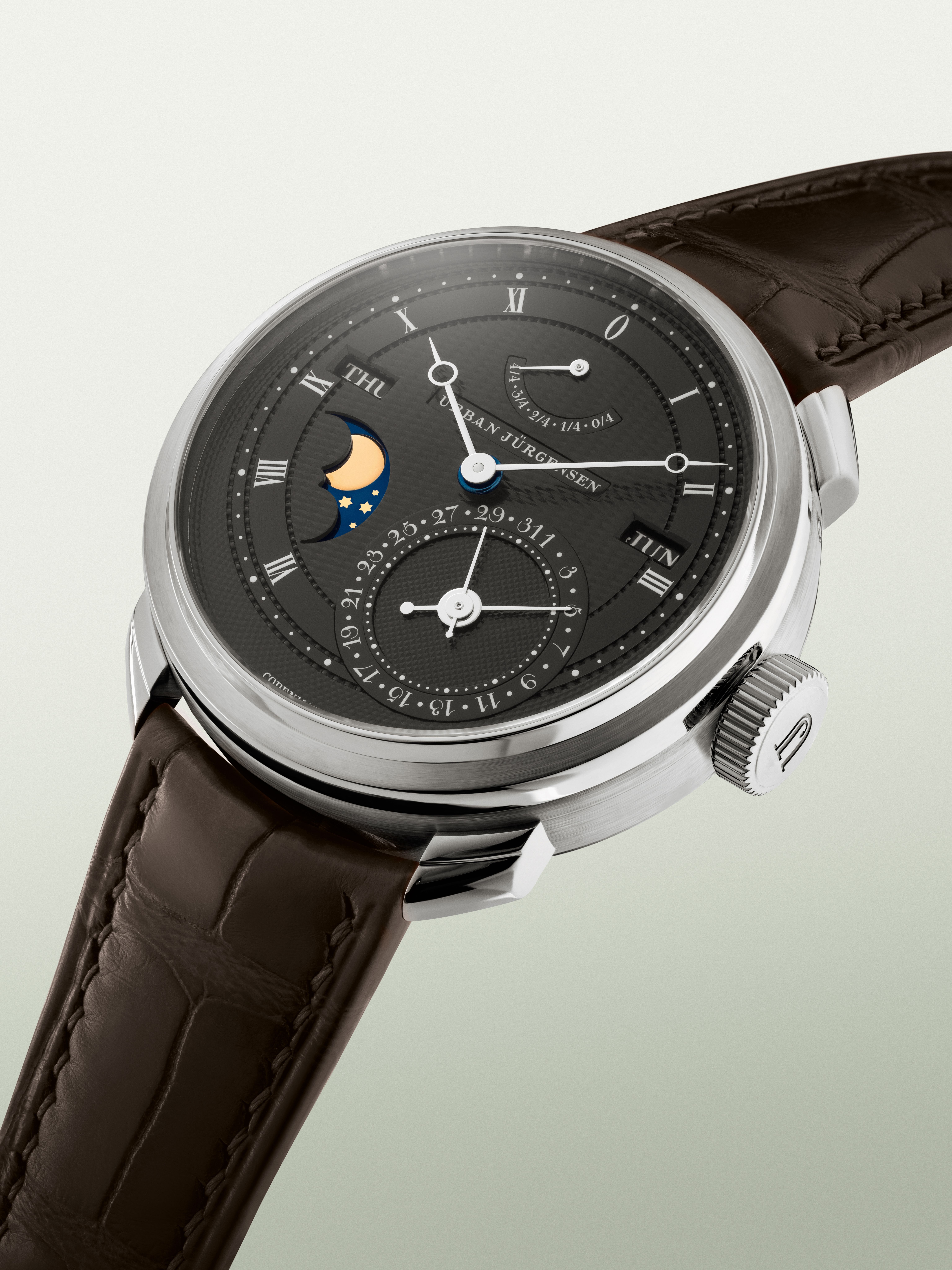 Platinum Urban Jürgensen wristwatch with dark guilloché dial, moonphase, day and date indicators, power reserve display, and brown leather strap.