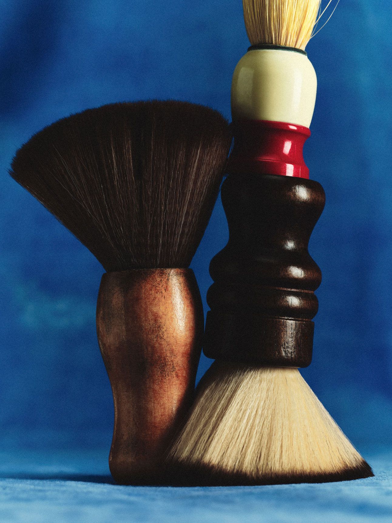 Two shaving brushes with wooden handles against a blue background.
