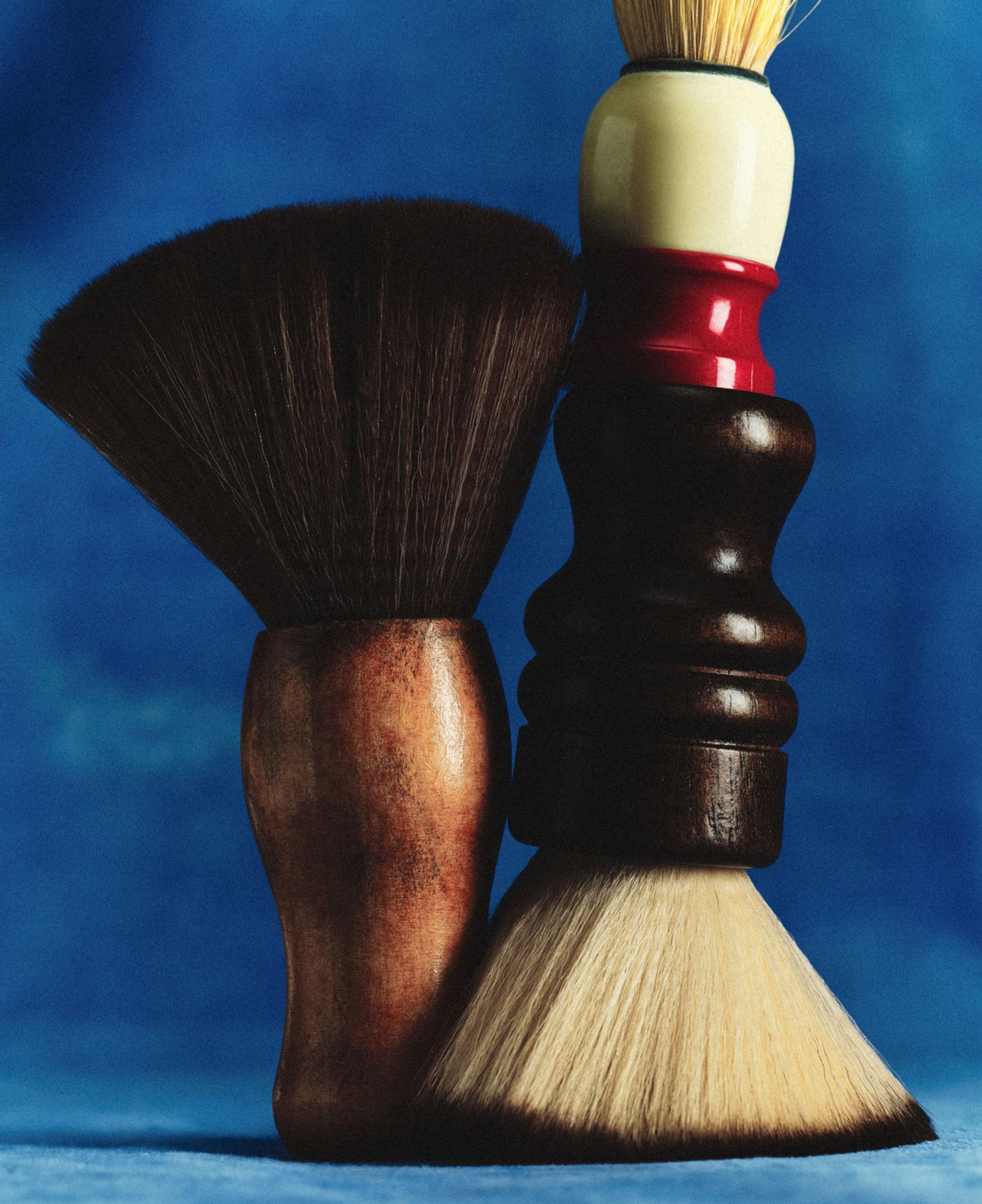 Two shaving brushes with wooden handles against a blue background.