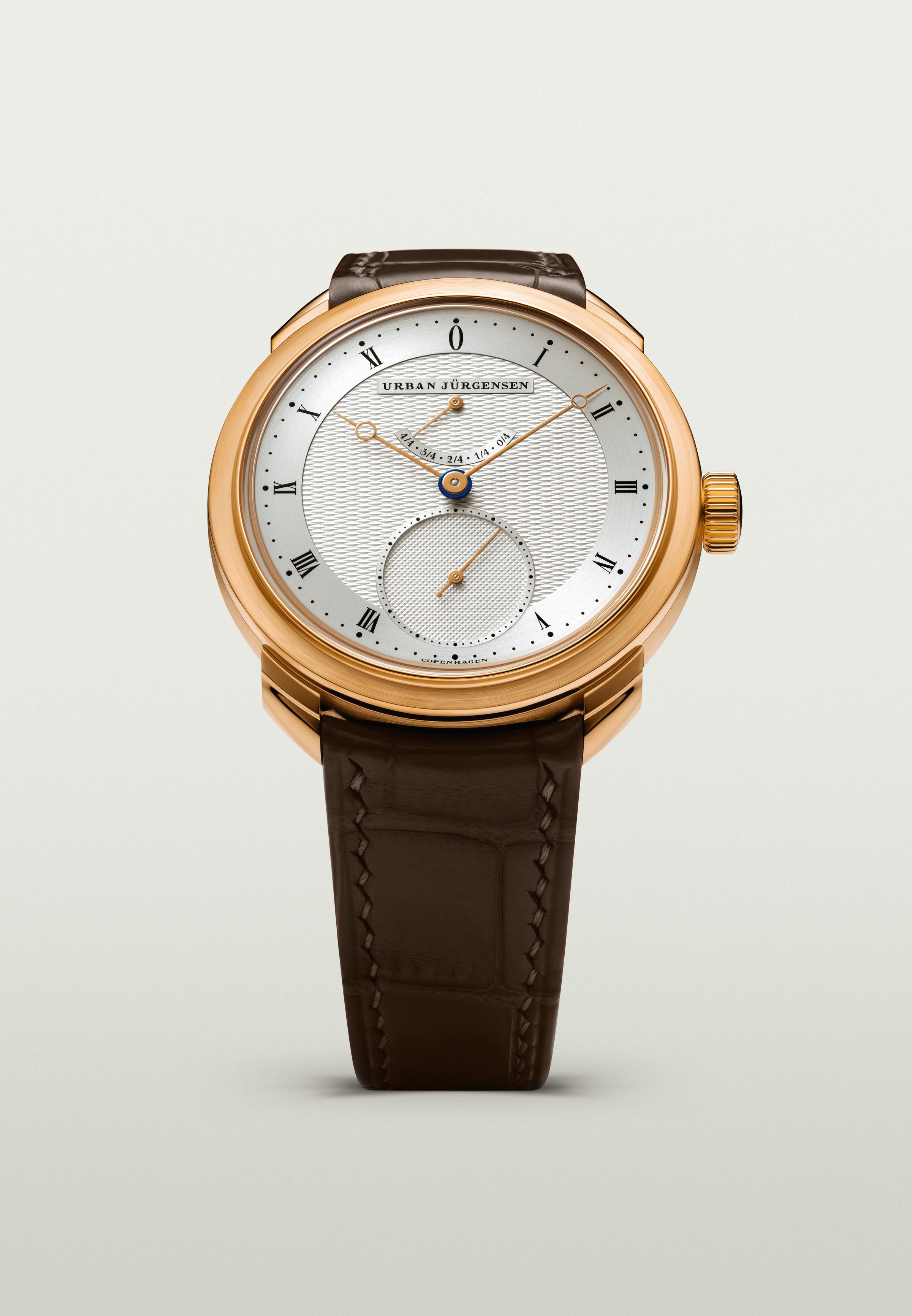 Front view of a rose gold Urban Jürgensen watch with silver guilloché dial, gold hands, power reserve indicator, and brown leather strap.