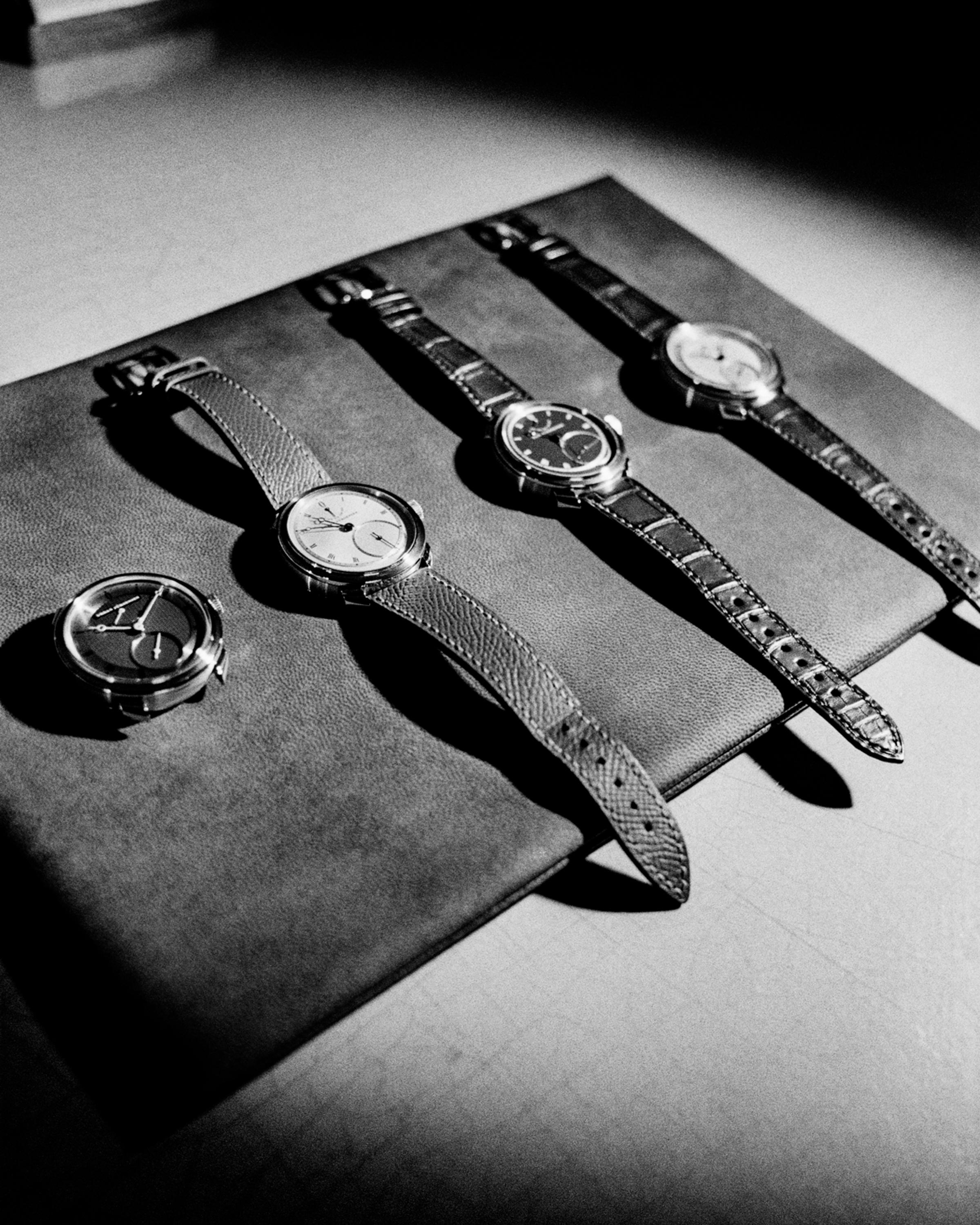 A black-and-white photo of four Urban Jürgensen wristwatches arranged on a leather mat