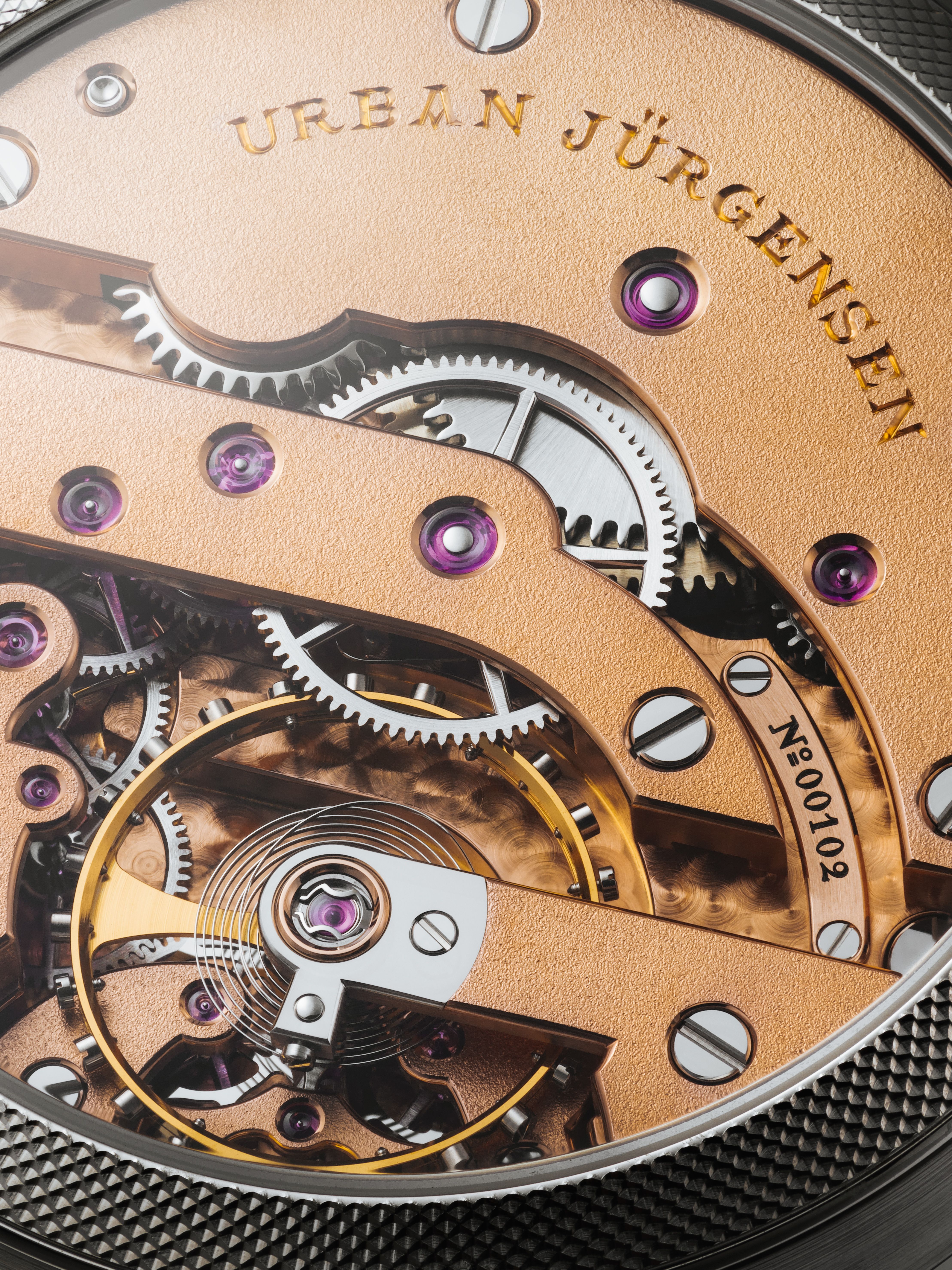 Close-up of a finely finished Urban Jürgensen watch movement showing gold-toned bridges, polished gears, ruby jewel bearings, and engraved serial number.
