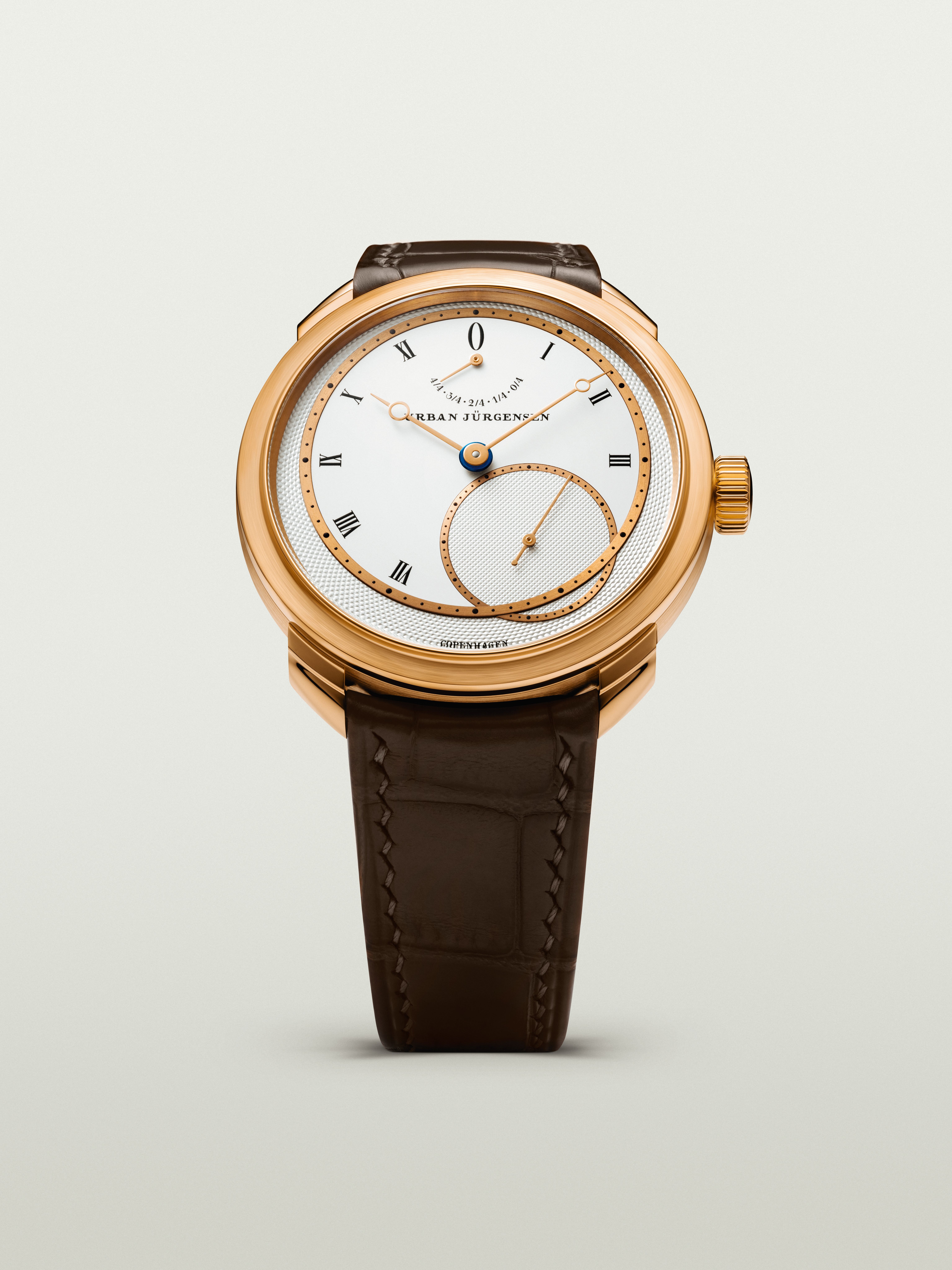 Rose gold Urban Jürgensen wristwatch with silver dial, gold hands, Roman numerals, power reserve indicator, and brown leather strap.