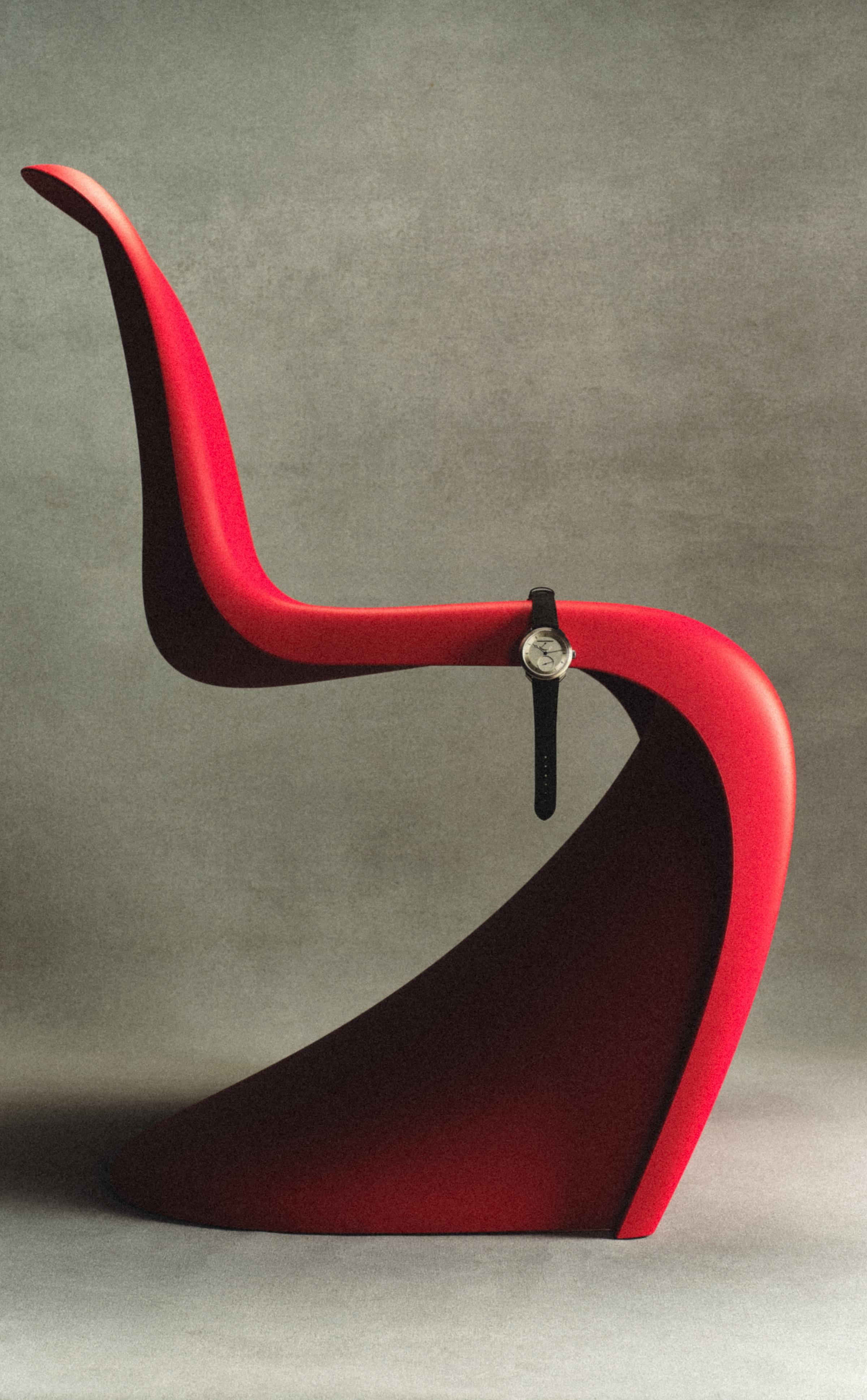 A red modern chair with a wristwatch draped over the curved seat edge.