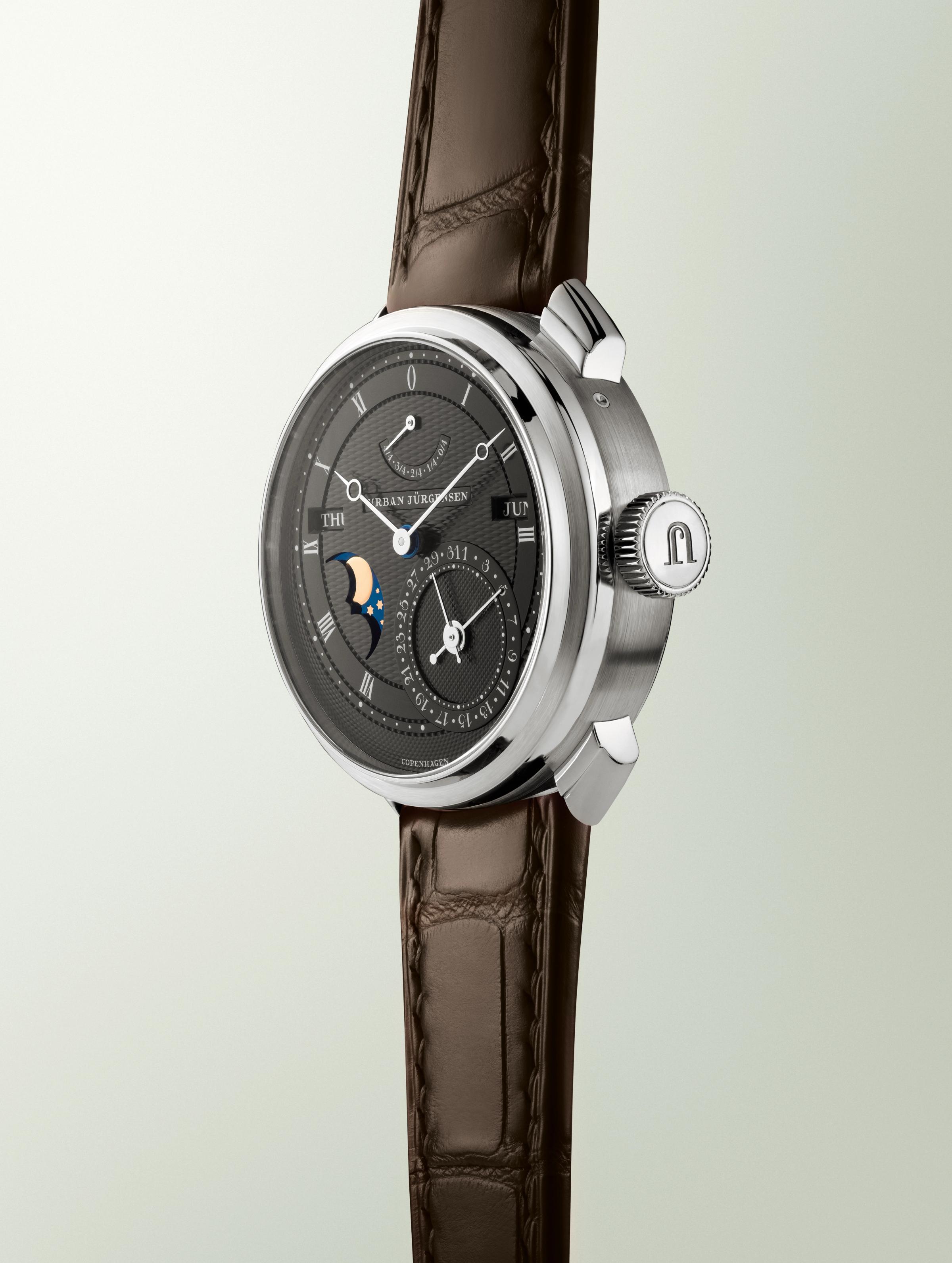 Platinum Urban Jürgensen wristwatch with dark guilloché dial, moonphase, day and date indicators, power reserve display, and brown leather strap.