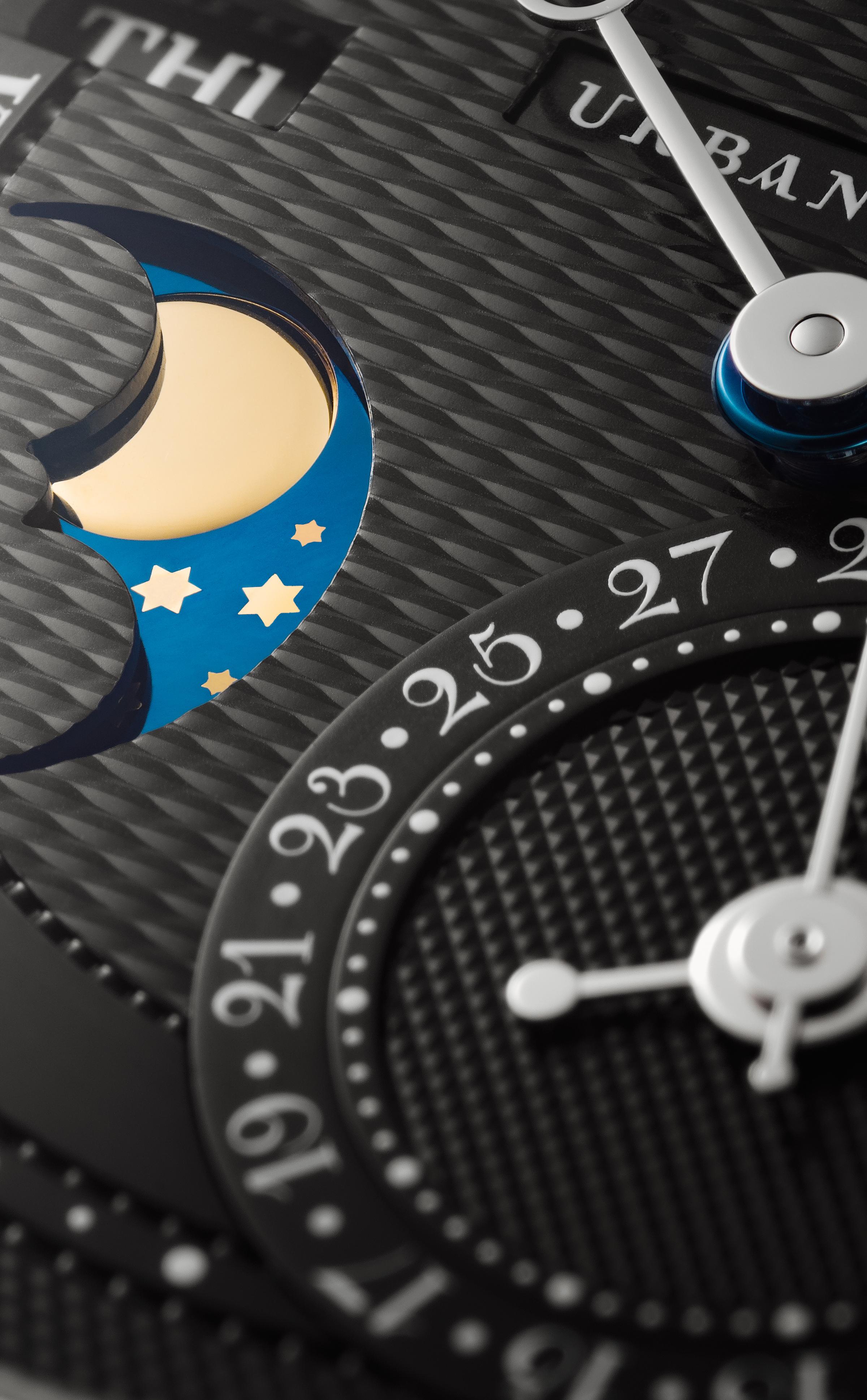 Close-up of a black guilloché watch dial featuring a moonphase display with gold moon and stars on blue, date subdial, day window, and polished hands.
