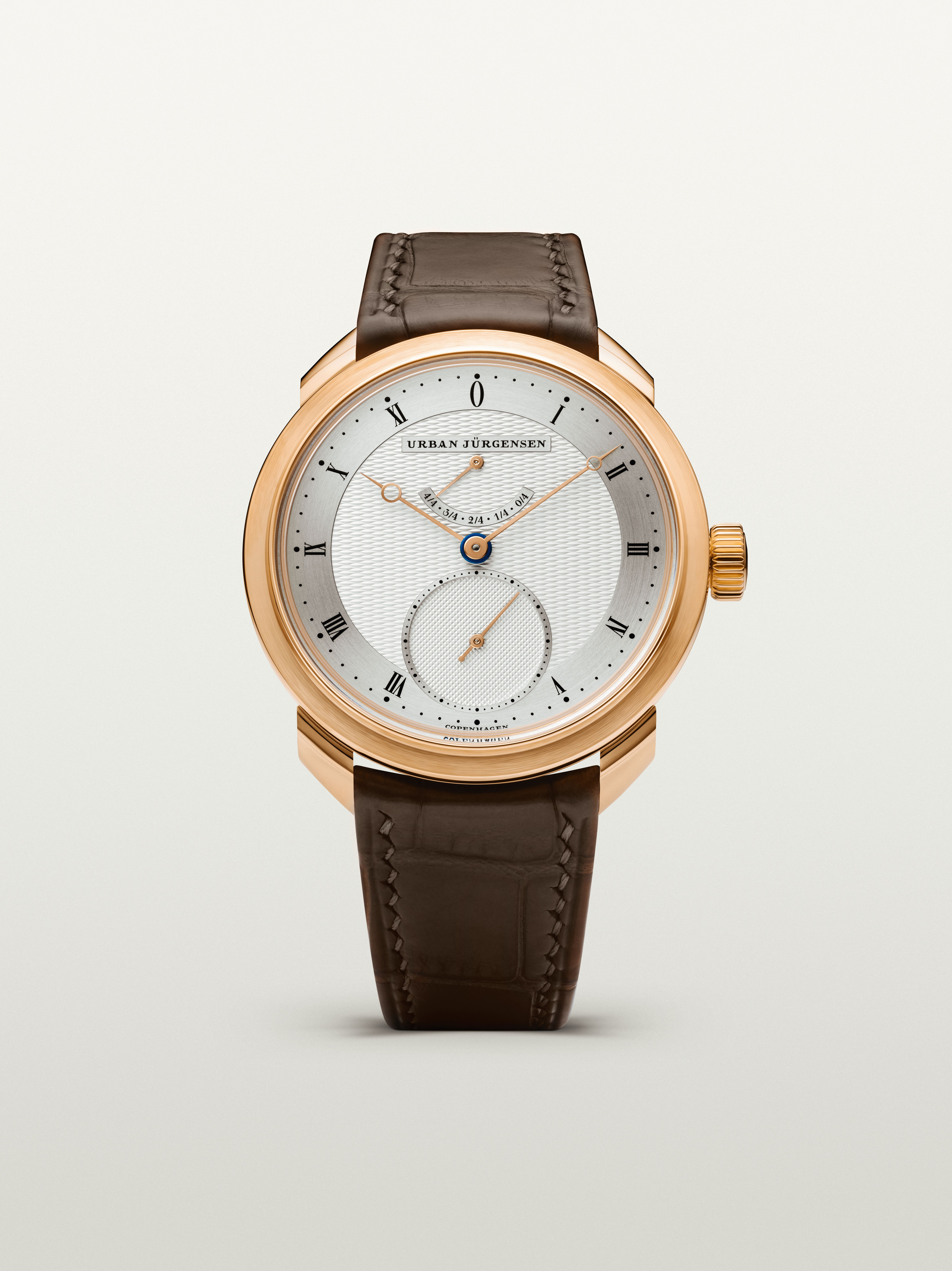 Rose gold Urban Jürgensen watch with guilloché silver dial, gold hands, power reserve, and brown leather strap.