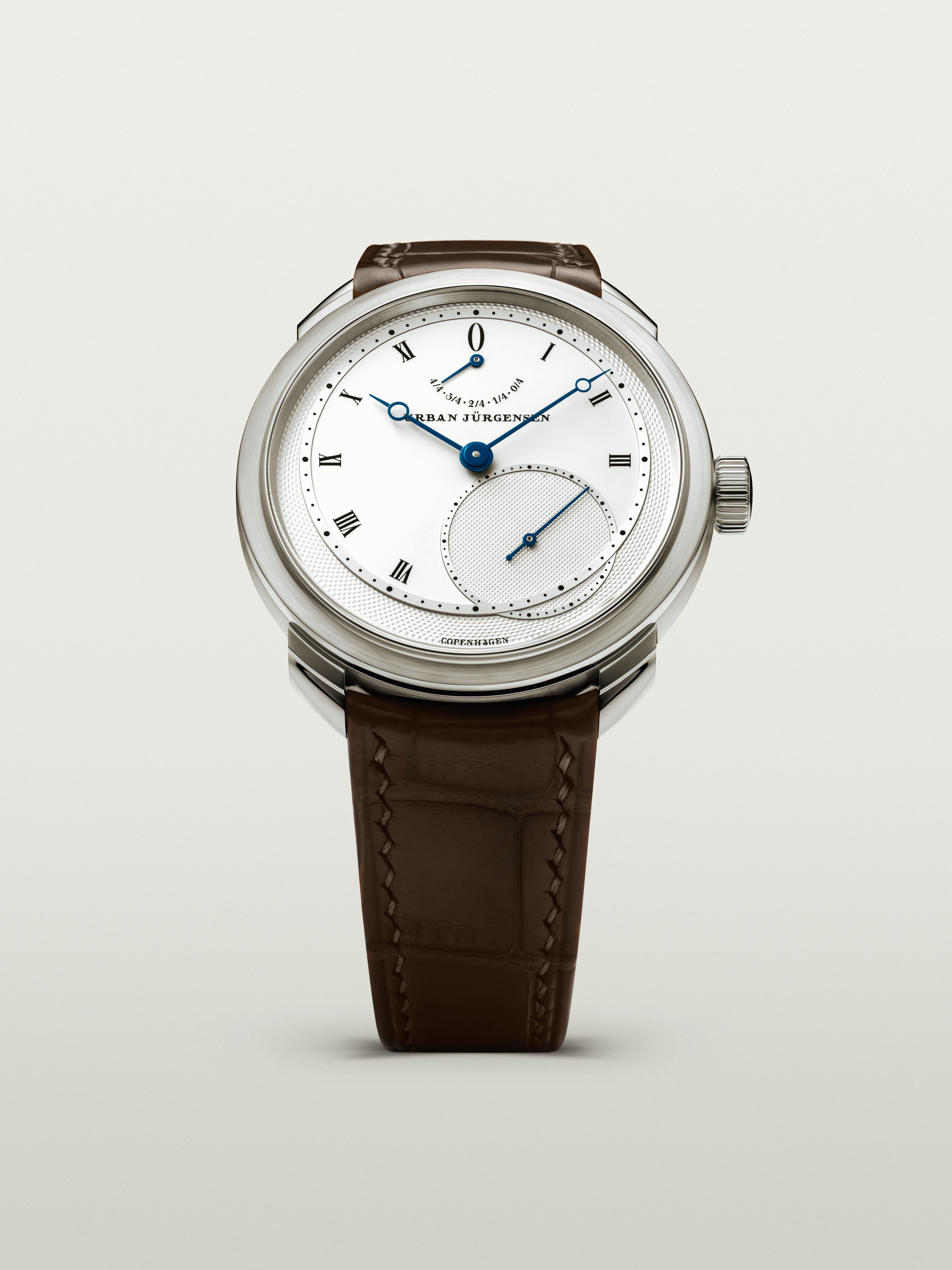 Platinum Urban Jürgensen wristwatch with silver dial, blued hands, Roman numerals, power reserve indicator, and brown leather strap.