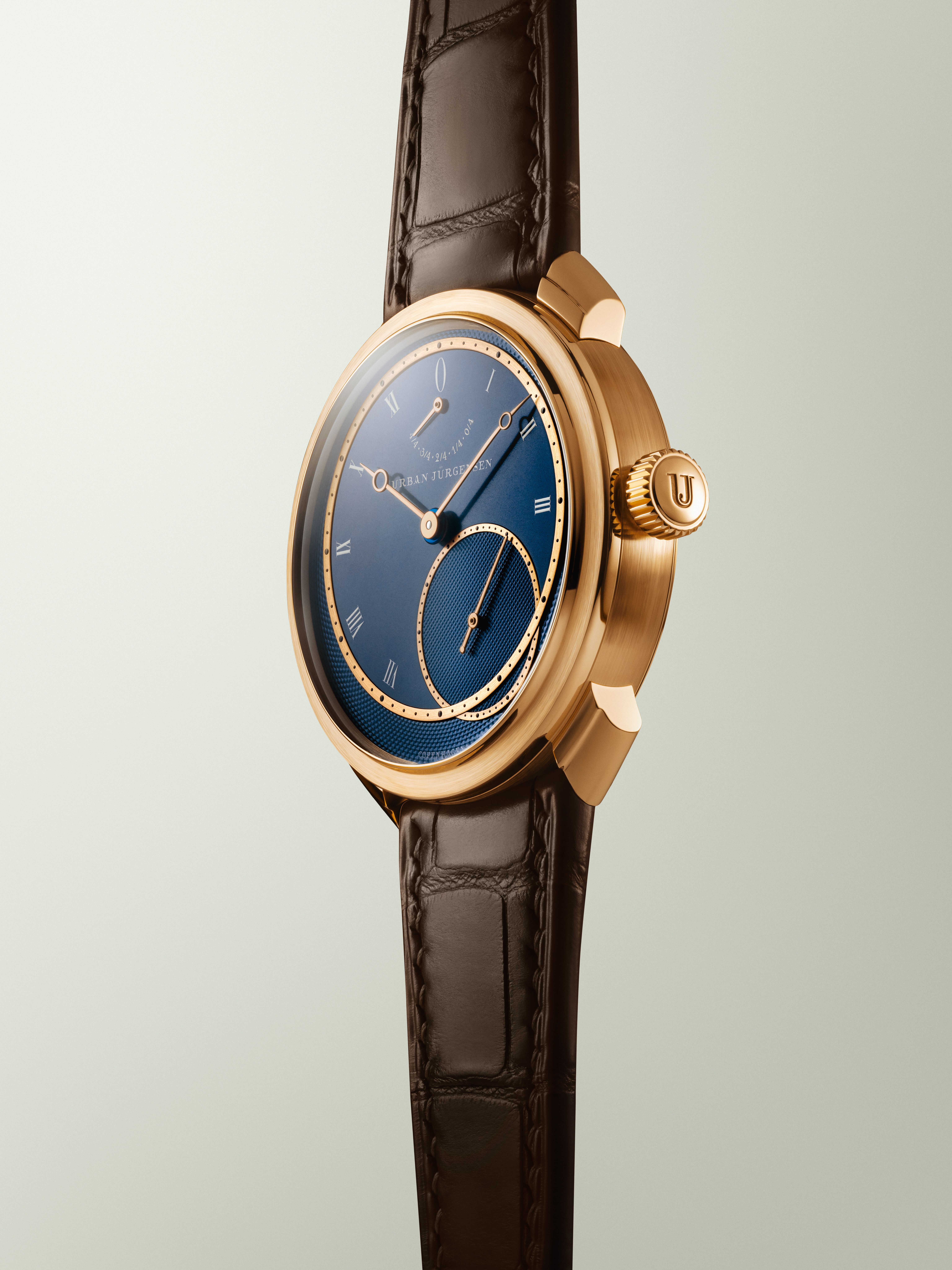 Rose gold Urban Jürgensen wristwatch with deep blue guilloché dial, Roman numerals, power reserve indicator, and brown leather strap.