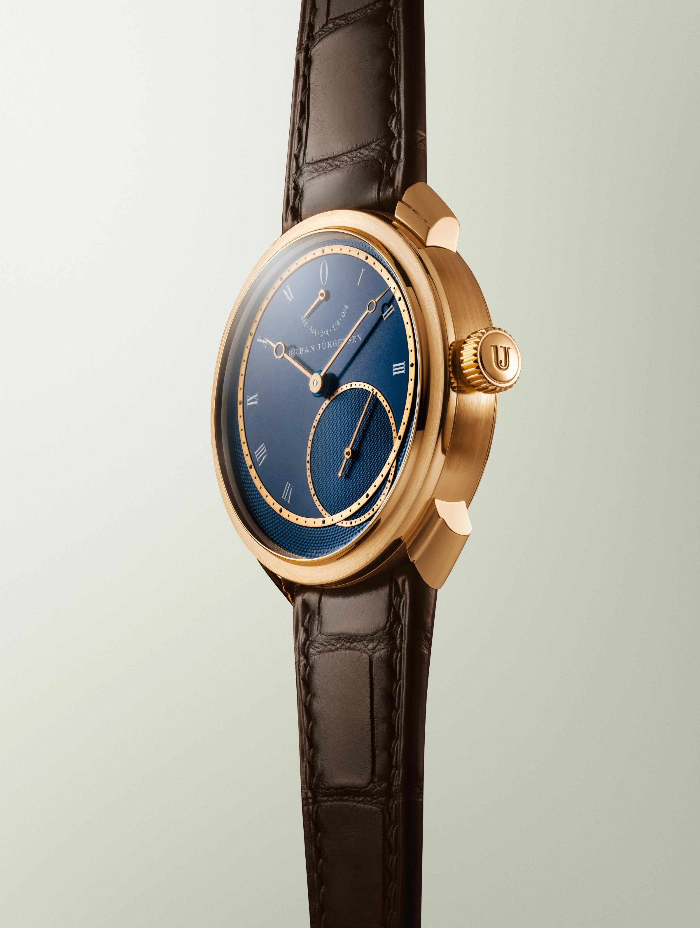 Rose gold Urban Jürgensen wristwatch with deep blue guilloché dial, Roman numerals, power reserve indicator, and brown leather strap.